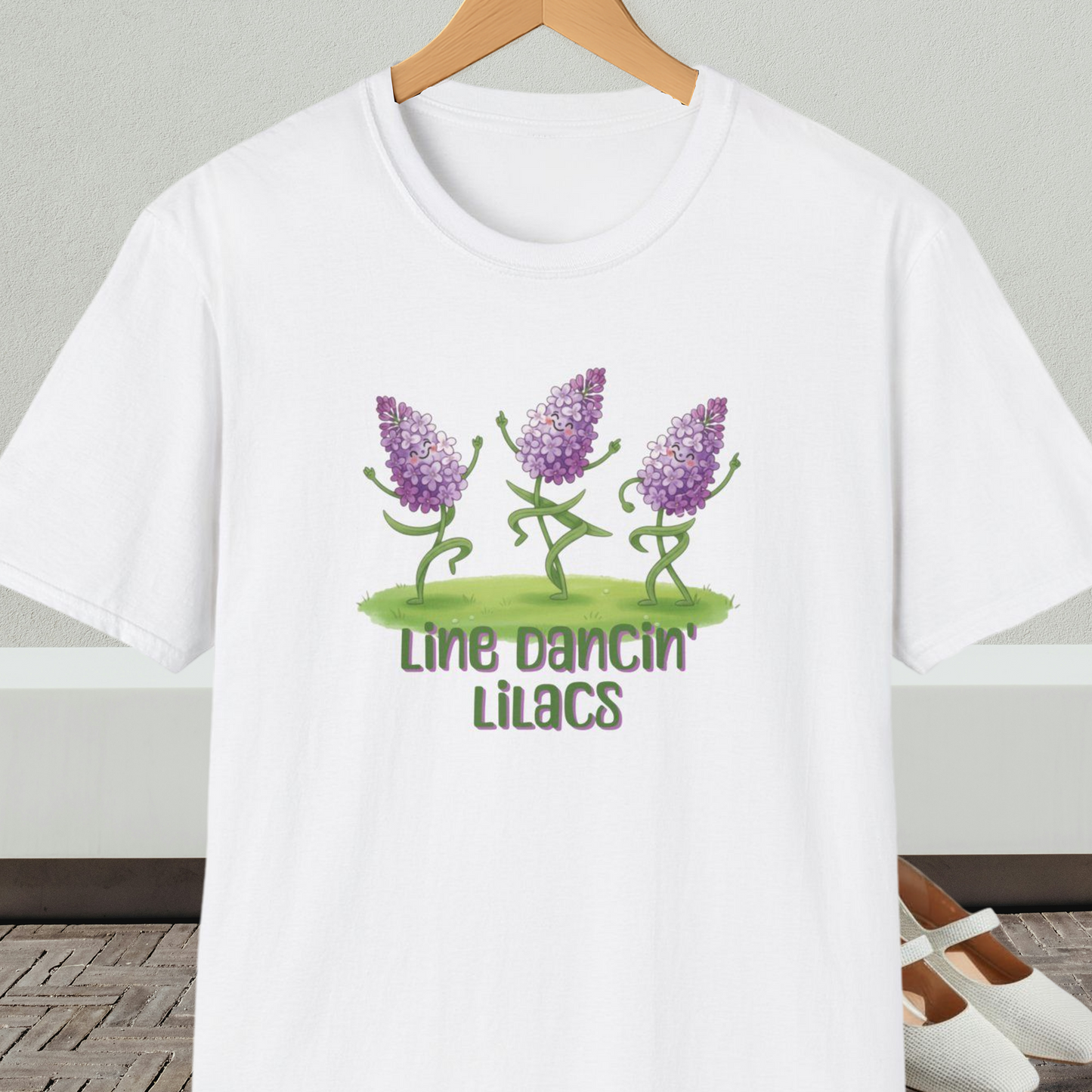 White t-shirt with text 'Line Dancin' Lilacs' and dancing flowers cartoon design.