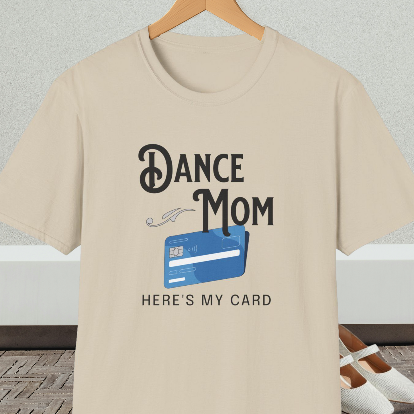 Beige t-shirt with 'Dance Mom, Here's My Card' text and credit card graphic, on a hanger with a neutral background.