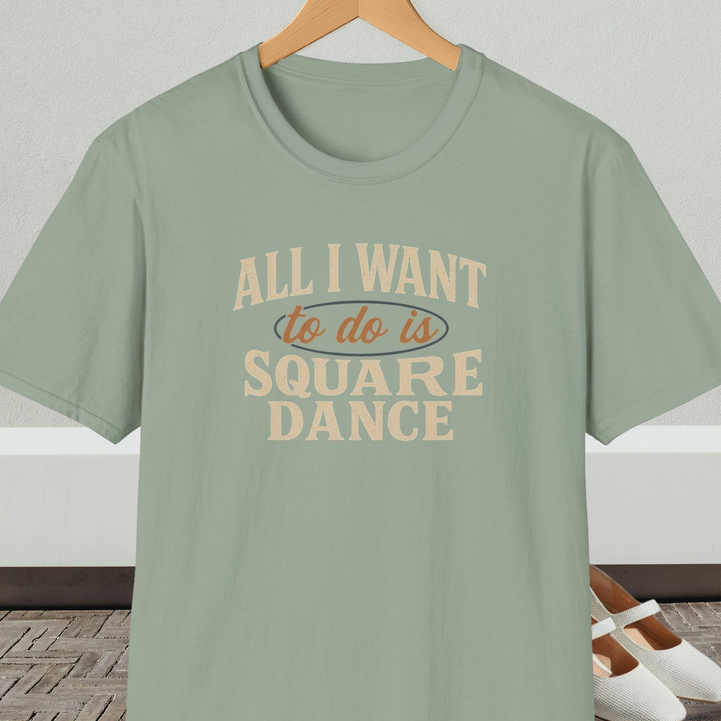 Sage green t-shirt with text 'All I Want to do is Square Dance' on a hanger against a neutral background.