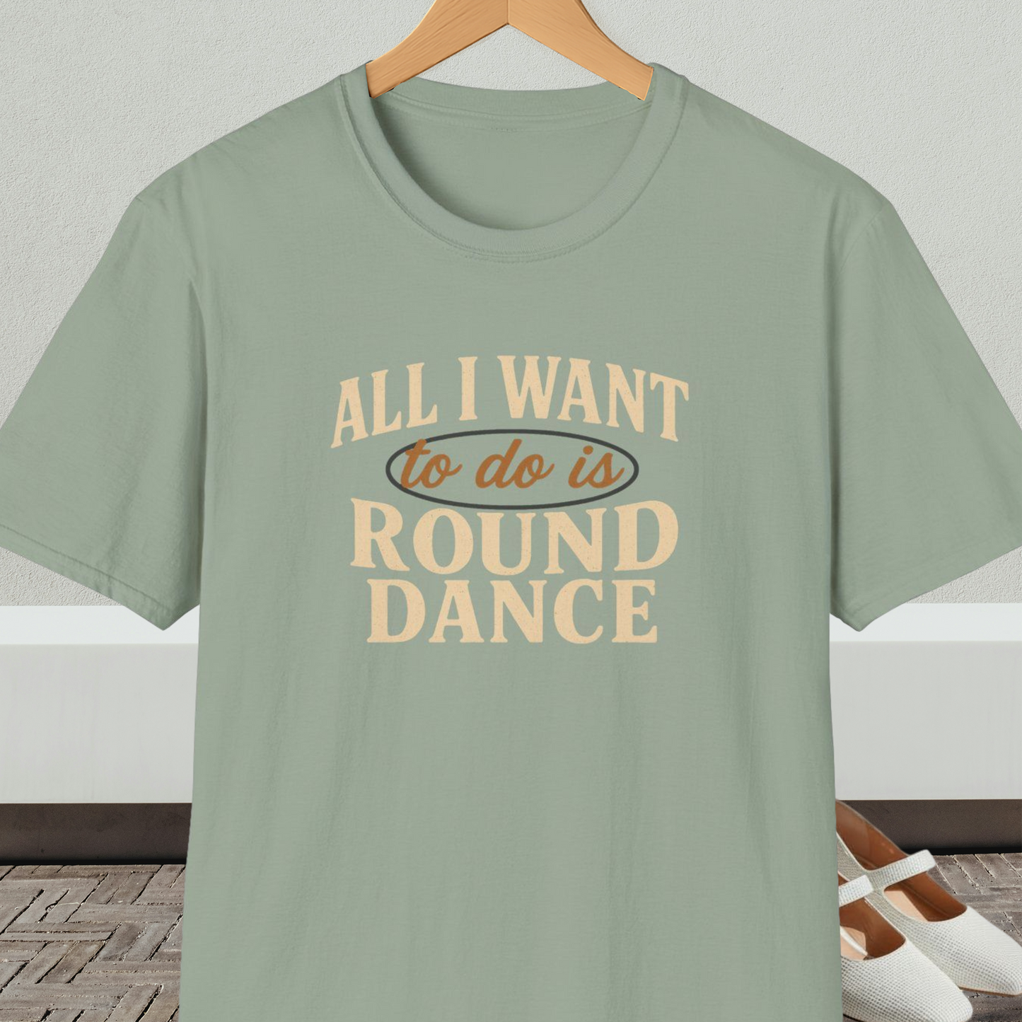 Sage green t-shirt with text 'All I Want to do is Round Dance' on a hanger against a neutral background.